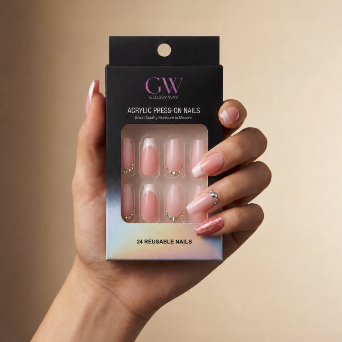 A hand holding a black box of glossy press-on nails. The nails are a soft nude pink with some decorated with small gold rhinestones and one with a silver rhinestone accent.