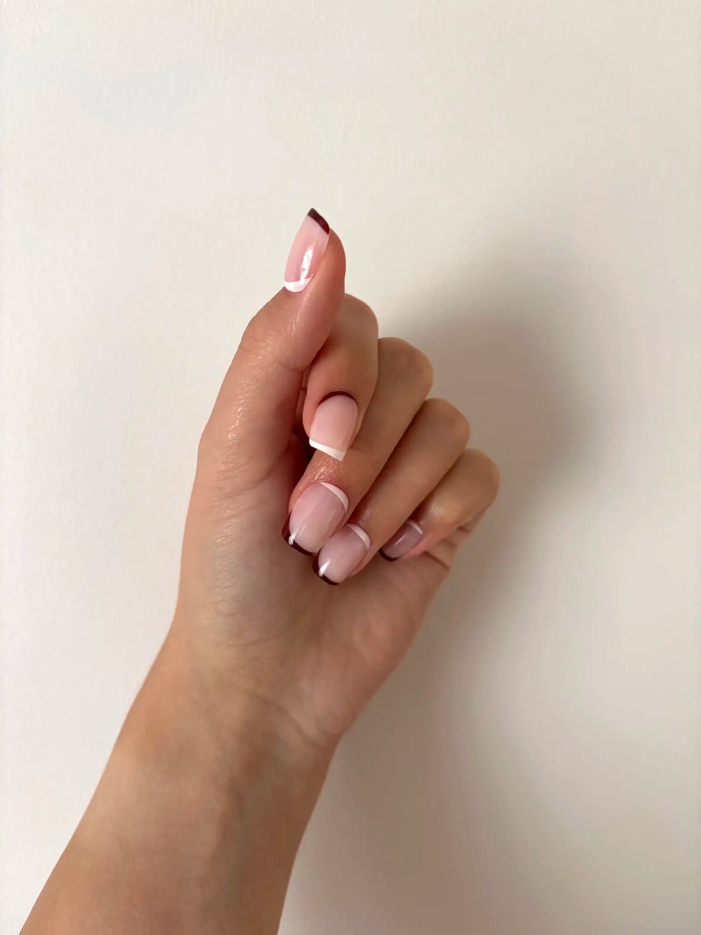 Close-up of a hand with pink brown french tip press on nails on a plain background
