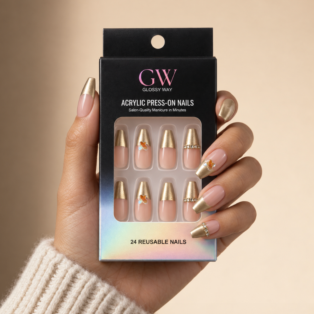 A hand wearing a set of glossy press-on nails holds a black box labeled GW Glossy Way Acrylic Press-On Nails. The nails are nude pink with metallic gold tips and small decorative gold and rhinestone accents.