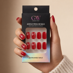 A hand wearing glossy red press-on nails with white starburst designs holds a black retail box labeled GW Glossy Way Acrylic Press-On Nails. The box has a holographic lower edge and shows 8 sample nails in the window packaging.