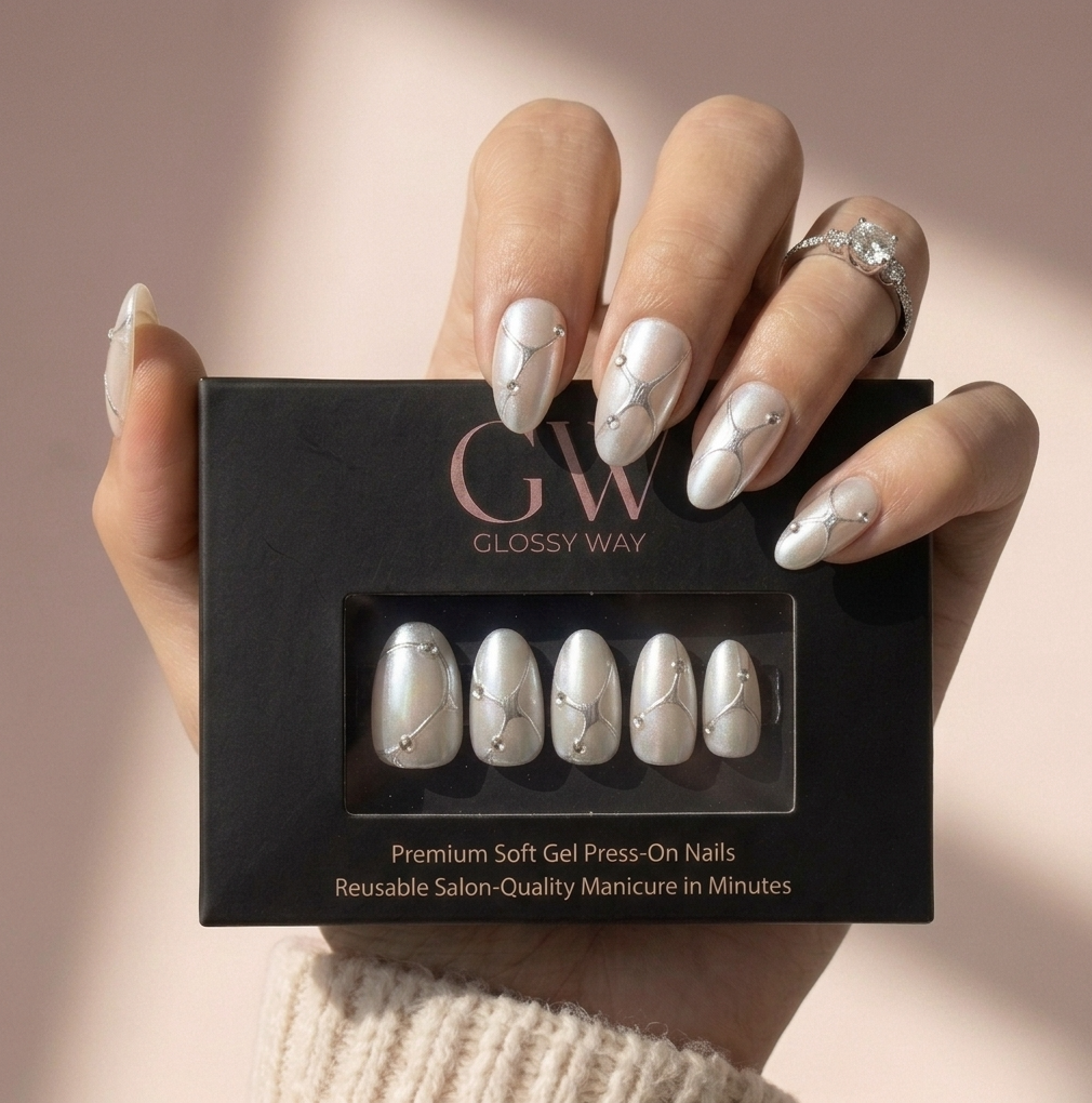 A hand holding a black box of Glossy Way press-on nails. The nails are glossy white with delicate silver glitter swirls and small rhinestone accents.