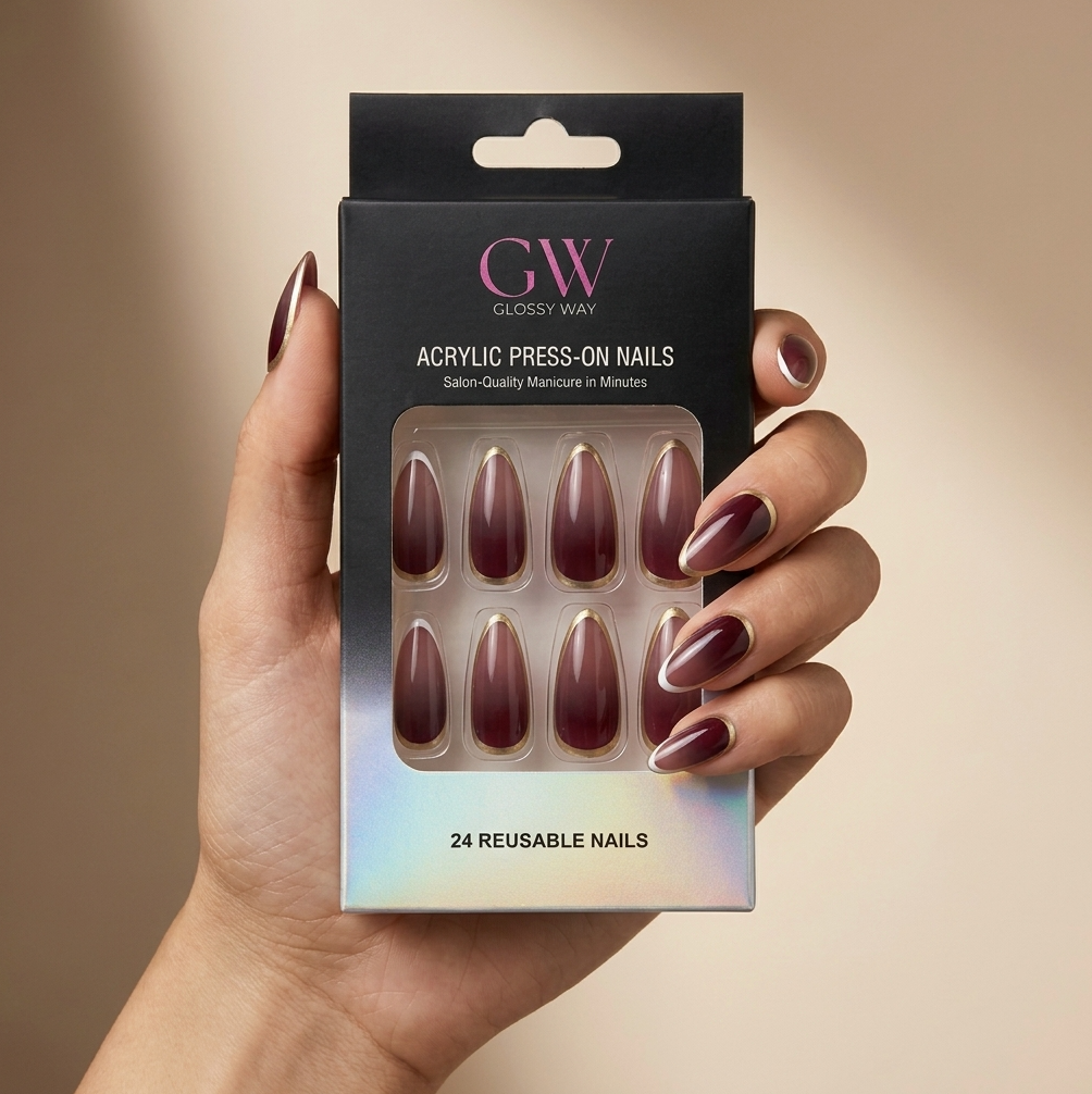 A hand holding a black box of GW Glossy Way press-on nails. The nails are a deep burgundy with a metallic gold accent at the tip, and the hand is shown against a warm beige background.