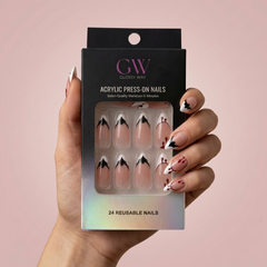 Mão a segurar uma caixa de unhas postiças acrílicas Glossy Way com base nude-rosa, manicura francesa preta e branca e detalhes vermelhos