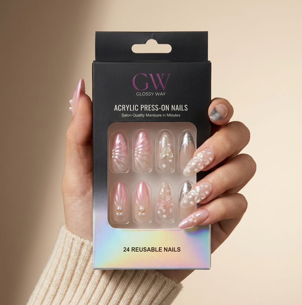 A hand wearing a beige knit sweater holds a black box of GW Glossy Way press-on acrylic nails. The nails are shown through a clear window on the packaging, featuring pink, nude, and white designs with pearl and glitter accents.