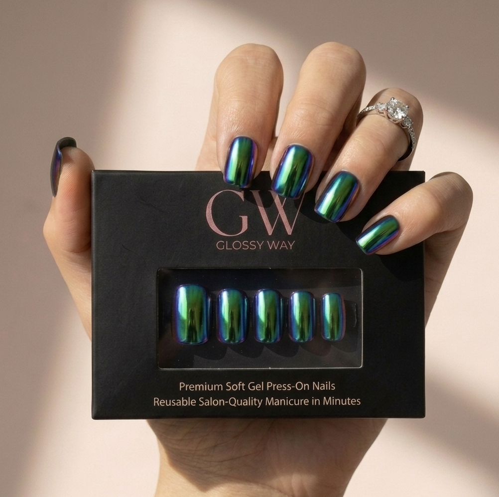 A hand holding a black box of Glossy Way press-on nails, with the nails displayed in a clear window on the box. The nails have an iridescent, holographic finish shifting between green, blue, and purple.