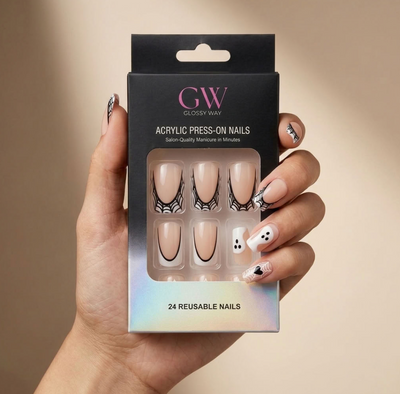 A hand holds a black box of GW Glossy Way press-on nails. The packaging is black with pink and white branding and a clear window showing nude beige nails with black spiderweb designs.